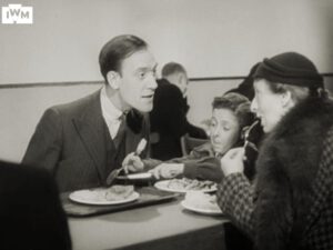 Tommy Trinder is focussed on explaining something to a woman at the table while a cheeky young scamp steals food from his plate