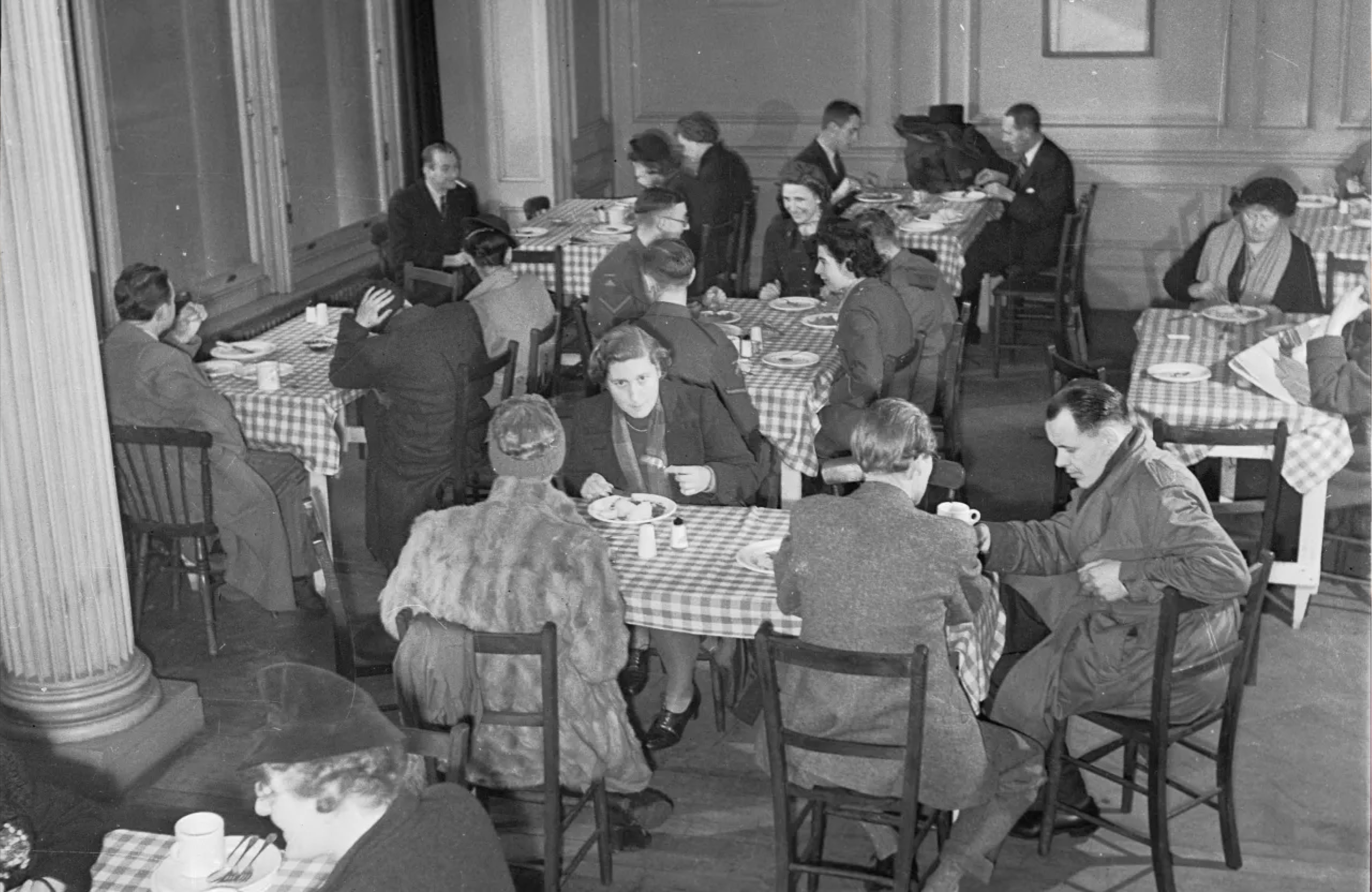 A busy cafe from the 1940's with customers sitting at tables eating their meals.