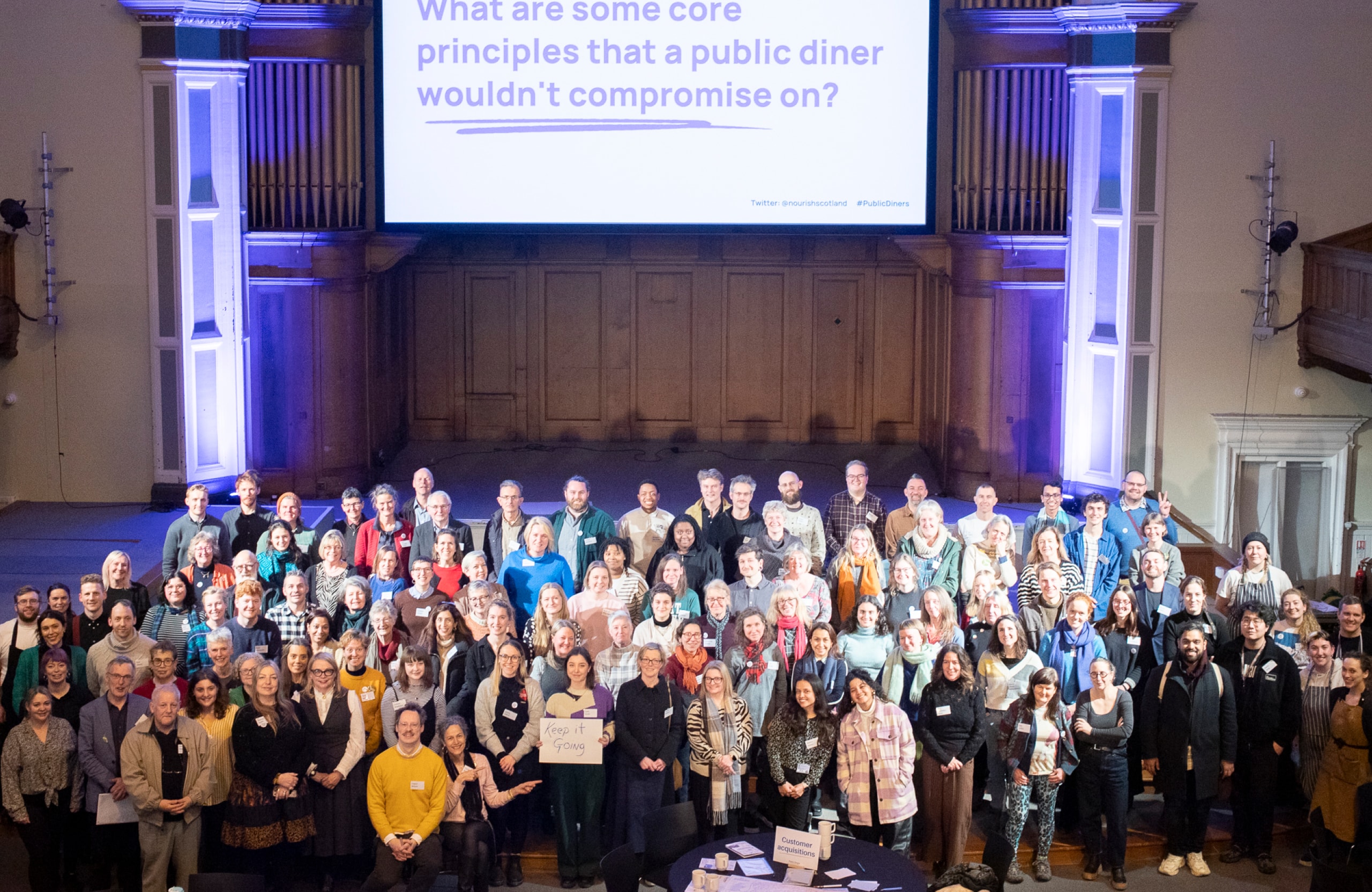 Large group of people assembled together under a large screen