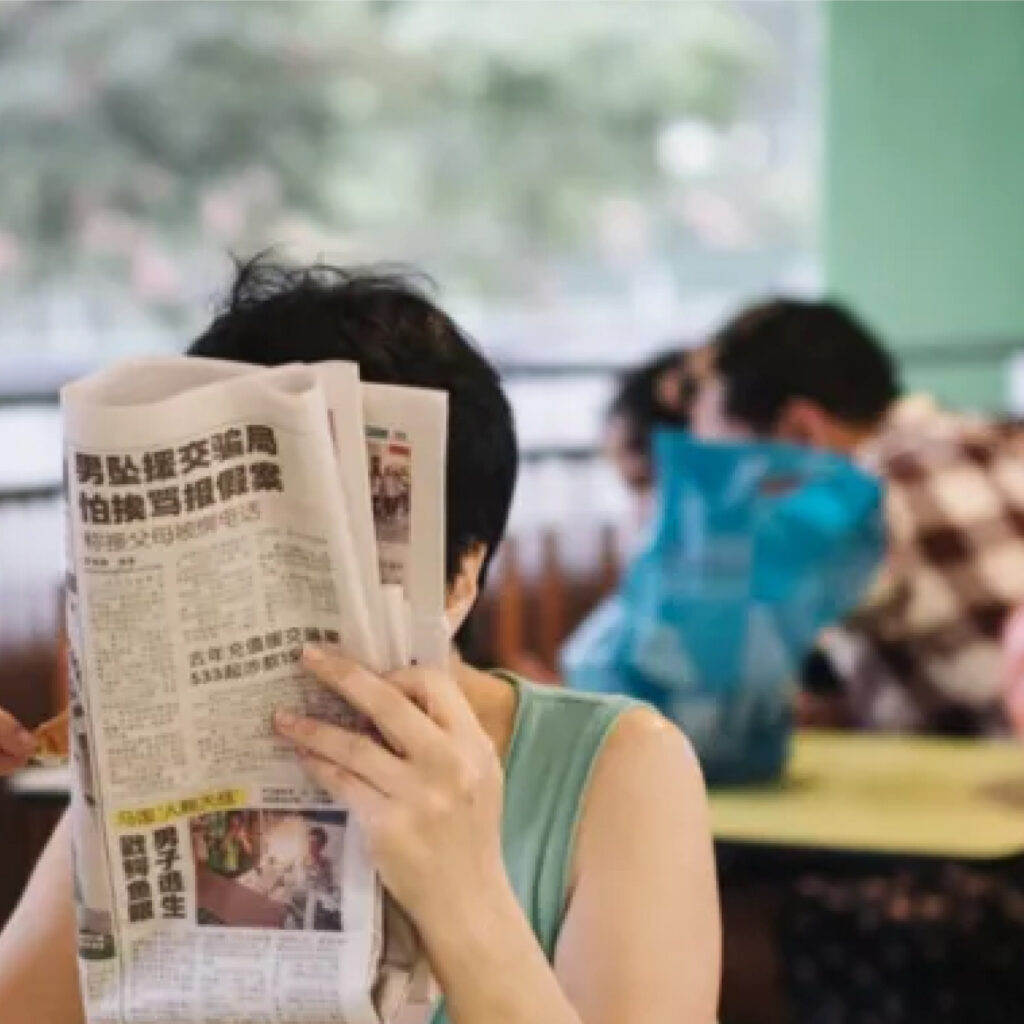 A woman relaxes at a public diner while reading the paper